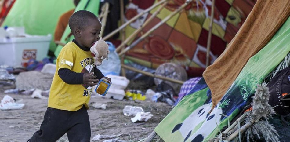 Un niño corre con comida que recibió de voluntarios en un campamento debajo del Puente Internacional Del Río donde se han alojado migrantes, muchos de Haití, después de cruzar el río Bravo, el jueves 23 de septiembre de 2021, en Del Río, Texas. (Foto AP/Julio Cortez)