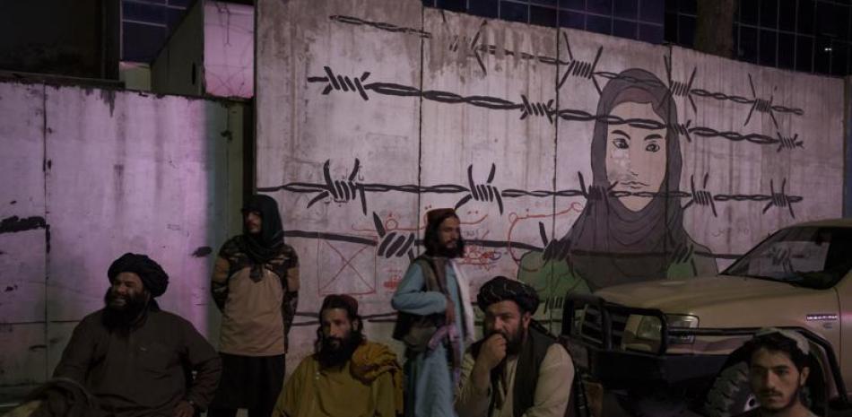 Miembros talibanes sentados frente a un mural que representa a una mujer detrás de un alambre de púas en Kabul, Afganistán, el martes 21 de septiembre de 2021. El lunes, los talibanes prohibieron a las barberías de una provincia del sur de Afganistán el afeitado o el recorte de la barba, alegando que su edicto está en consonancia con la sharía, o ley religiosa del islam. (AP Foto/Felipe Dana)