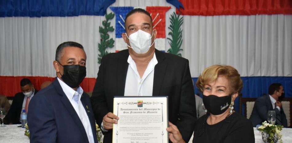 El periodista Tony Reyes recibe de Sonia María y Kelvin Grullón la resolución que lo declara como “Hijo Adoptivo” de este municipio.