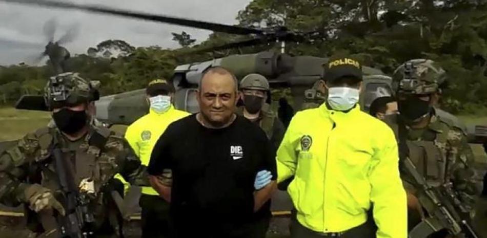 Se ve al capturado sonriente, vestido con pantalón y camiseta negra y con la manos atadas a la espalda, cuando es conducido por soldados armados con fusiles luego de bajar de un helicóptero militar. AFP
