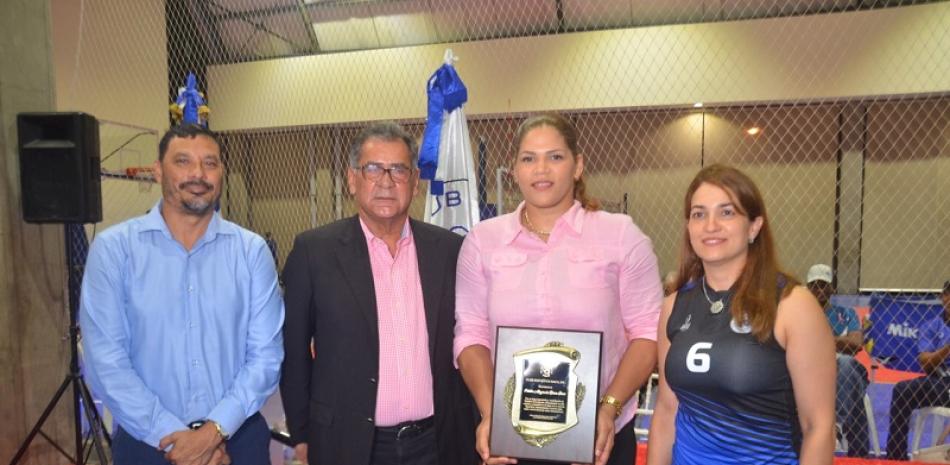 El presidente del Club Naco, doctor Luis Miguel Pou, y Audry Lehoux, entregan una placa de reconocimiento a Prisilla Rivera, exselección de voleibol