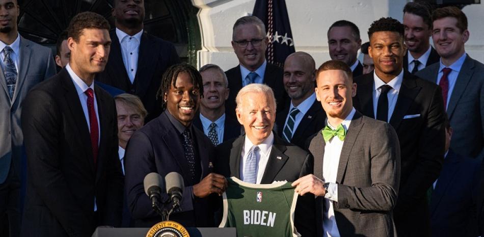 El presidente de Estados Unidos Joe Biden sostiene una camiseta de los Bucks junto a Jrue Holiday y Donte DiVincenzo durante la visita de los campeones de la NBA.