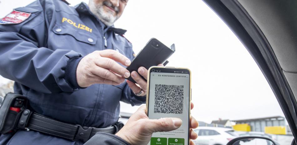 Un oficial de policía austriaco verifica el certificado de vacunación digital de un conductor en un teléfono inteligente durante un control de tráfico en Graz, Austria. // AFP