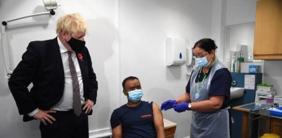 El primer ministro británico, Boris Johnson (izq.), Se encuentra junto a un hombre que recibe una vacuna de refuerzo COVID-19 durante una visita al centro de vacunación Woodgrange GP Surgery en el este de Londres el 15 de noviembre de 2021. // AFP