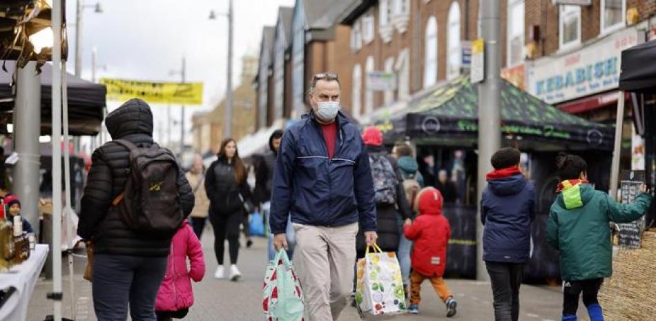 Un comprador que se cubre la cara para detener la propagación del COVID-19, lleva bolsas de la compra mientras pasa frente a los puestos en Walthamstow Market en el este de Londres el 21 de noviembre de 2021.

Foto: Tolga Akmen / AFP