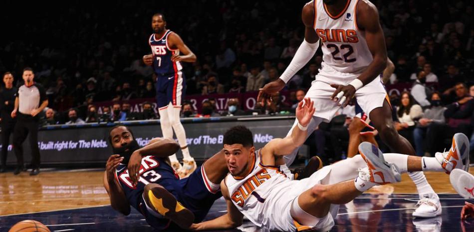 James Harden (13), de los Nets de Brooklyn, y Devin Booker (1), de los . Suns de Phoenix, disputan el balón en el suelo en la segunda mitad del partido de la NBA, en Nueva York.