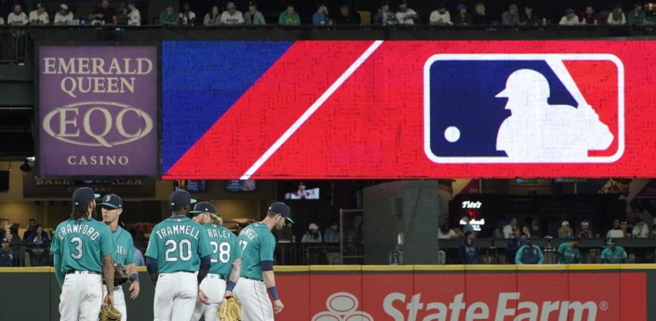 En esta imagen de archivo, los jugadores de los Marineros de Seattle esperan mientras una pantalla muestra el logo de la MLB durante la revisión de una jugada en el noveno inning de un juego que enfrentó al equipo con los Rays de Tampa Bay, el 18 de junio de 2021, en Seattle.