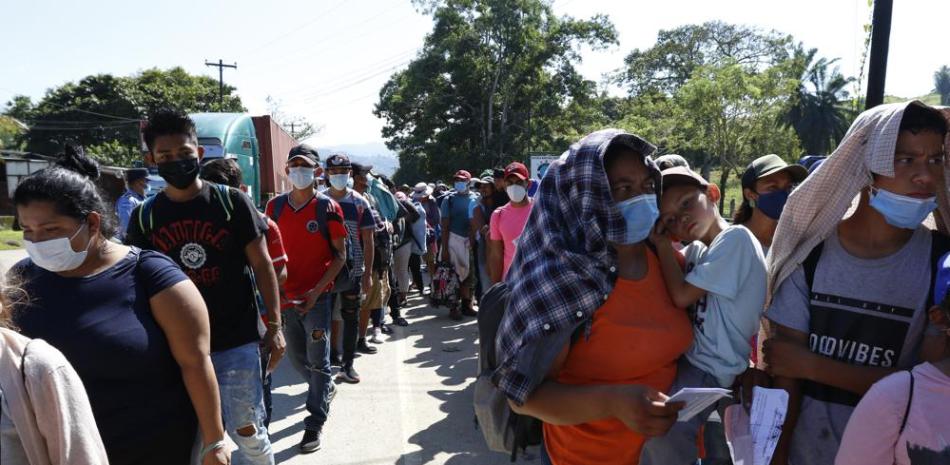 Migrantes que forman parte de una caravana que aspira con llegar a Estados Unidos esperan en una línea para que agentes de la policía revisen su documentación en Corinto, Honduras, el sábado 15 de enero de 2022. (AP Foto/Delmer Martínez)