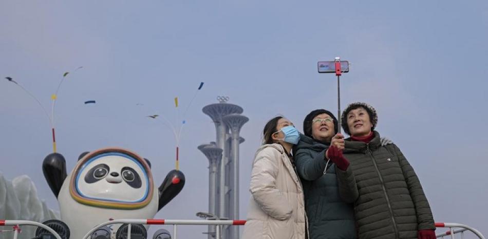 Una mujer porta una máscara mientras se toma una fotografía con otras personas frente a la mascota de los Juegos Olímpicos de Invierno de Beijing.