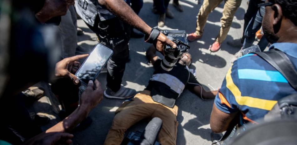 Miembros de los medios de comunicación rodean el cuerpo de un periodista en el suelo después de que resultó fatalmente herido luego de una protesta de los trabajadores de una fábrica que exigían un aumento salarial, en Puerto Príncipe, Haití, el 23 de febrero de 2022. 

Foto: Richard Pierrin / AFP