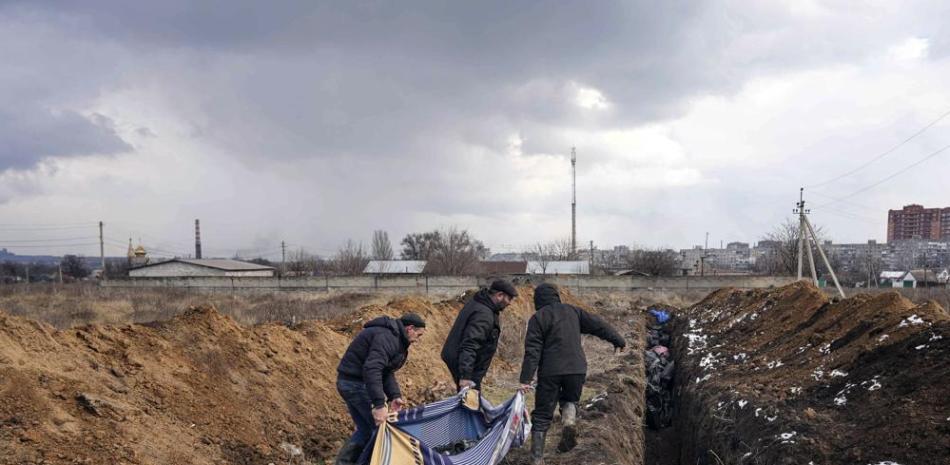 Tres individuos arrastran cadáveres a ser depositados en una larga fosa común en las afueras de Mariúpol (Ucrania) el 9 de marzo del 2022. (AP Photo/Evgeniy Maloletka)