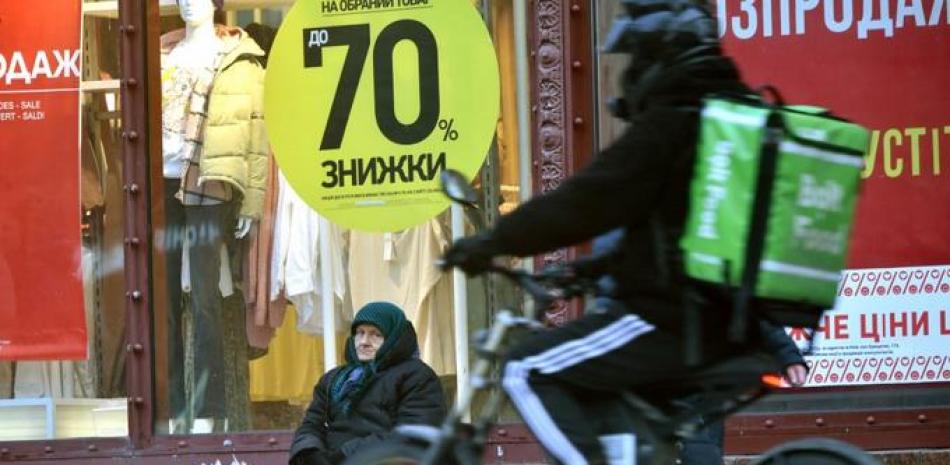 Una anciana vende flores frente a un escaparate con un cartel que dice "Descuentos del 70%" en el centro de la capital ucraniana de Kiev el 2 de febrero de 2022. Foto: AFP