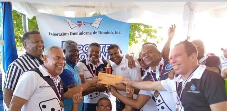 Roberto Neris (con t-shirt azul), director de Deportes de la Alcaldía de Santo Domingo Este, y Roberto Parra (izquierda), presidente de la Federación Dominicana de Dominó, premian al mánager del equipo campeón, Gerald Colón, junto a los jugadores.