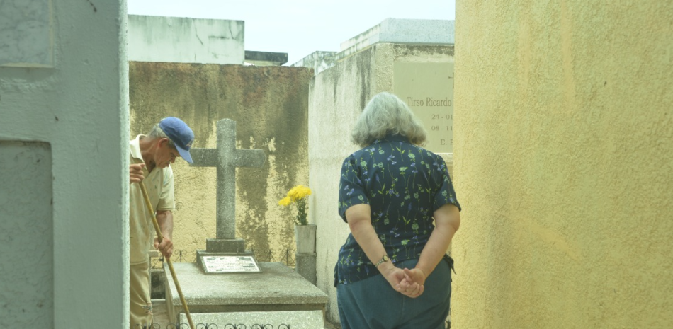 Arriba, una dama espera por la limpieza de la tumba de su familiar.