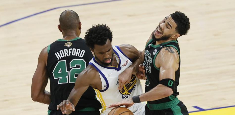 Andrew Wiggins, al centro, de los Warriors, se queda con el balón al pasar entre Al Horford (42) y Jayson Tatum de los Celtics en el quinto partido de las finales de la NBA.
