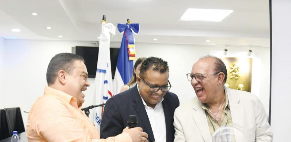 Chucky Acosta no esconde la felicidad al recbir la placa de reconocimiento de manos del director de la ONDA, acompañado de Pochi Familia.