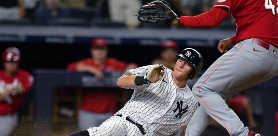 El jugador de los Yanquis DJ LeMahieu se desliza junto al pitcher de los Rojos de Cincinnati Alexis Díaz para anotar en un wild pitch en el 10mo inning.