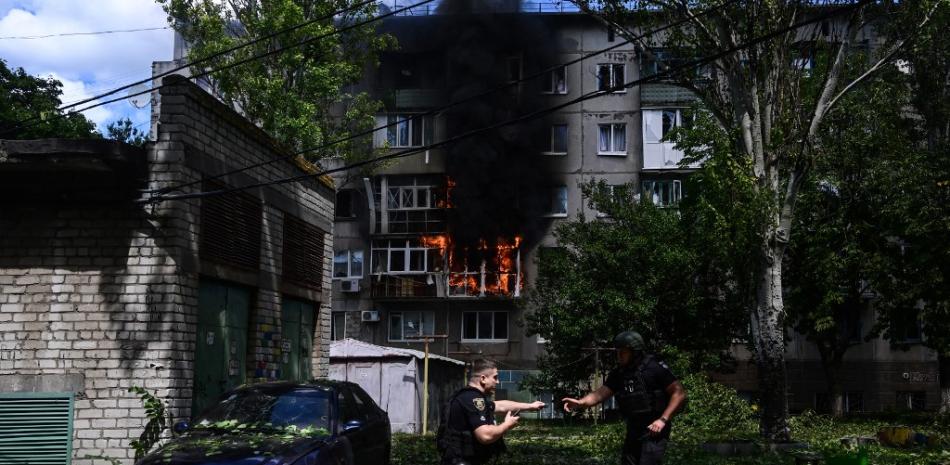 Policías reaccionan junto a un herido que yace en el suelo frente a un edificio en llamas después de que un ataque aéreo impactara en el patio de unas residencias civiles en el centro de Kramatorsk, en el este de Ucrania, el 19 de julio de 2022, en medio de la invasión rusa de Ucrania. Foto: Miguel Medina/AFP.