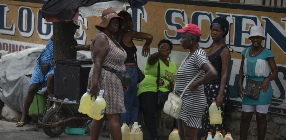Varias mujeres muestran su incomodidad mientras son fotografiadas vendiendo gasolina de contrabando en jarras de plástico de un galón en Puerto Príncipe, ayer. AP