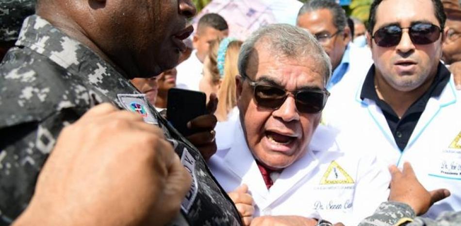 El presidente del Colegio Médico Dominicano, Senén Caba, es contenido por fuerzas policiales mientras encabazaba ayer una marcha que fue impedida de llegar al Palacio Nacional, para demandar al gobierno del presidente Luis Abinader una serie de reivindicaciones en el sector de la salud.  José  A. Maldonado