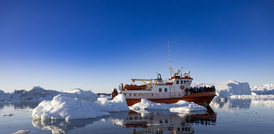 En esta foto de archivo tomada el 1 de julio de 2022, un bote que transportaba turistas maniobra entre icebergs que flotan en Disko Bay, Ilulissat, al oeste de Groenlandia. Un número creciente de turistas de todo el mundo acuden en masa a Groenlandia para admirar los impresionantes icebergs, las vastas vistas y la belleza natural de la isla ártica. Pero las autoridades ahora están considerando formas de controlar el número de multitudes para proteger el frágil medio ambiente, que ya está amenazado por el calentamiento global. Odd ANDERSEN / AFP