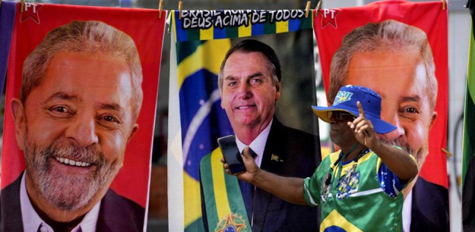Un manifestante vestido con los colores de la bandera brasileña pasa frente un vendedor de banderas con las imágenes de Lula y Bolsonaro, el martes pasado. ap