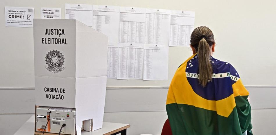Una mujer envuelta en una bandera brasileña vota en un centro de votación durante las elecciones legislativas y presidenciales en Brasilia, Brasil, el 2 de octubre de 2022. La votación comenzó el domingo temprano en la economía más grande de América del Sur, plagada de desigualdades y violencia, donde los votantes ar Se espera que elija entre el titular de extrema derecha Jair Bolsonaro y el favorito de izquierda Luiz Inácio Lula da Silva, cualquiera de los cuales debe obtener el 50 por ciento de los votos válidos, más uno, para ganar en la primera vuelta. EVARISTO SA / AFP