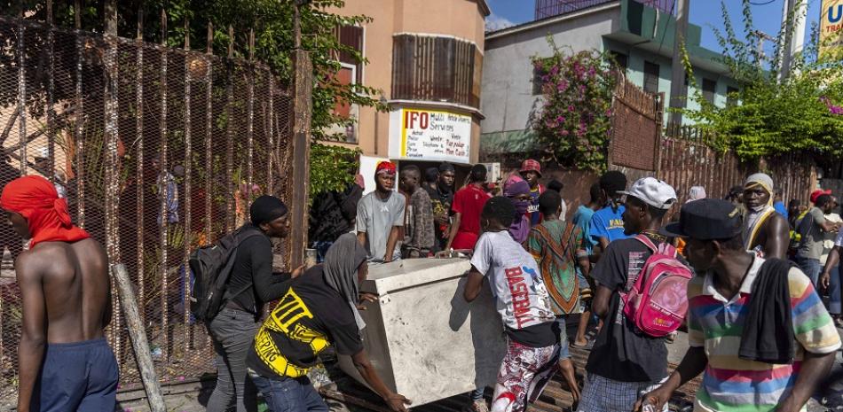 Los hombres huyen con propiedad saqueada durante una protesta contra el primer ministro haitiano Ariel Henry pidiendo su renuncia, en Port-au-Prince, Haití. AFP.
