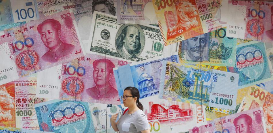 Una mujer pasa frente a una casa de cambio decorada con divisas de todo el mundo en Hong Kong el 6 de agosto del 2019. Un dólar fuerte respecto al resto de las divisas hace que aumenten las posibilidades de una recesión mundial. (AP Photo/Kin Cheung, File)