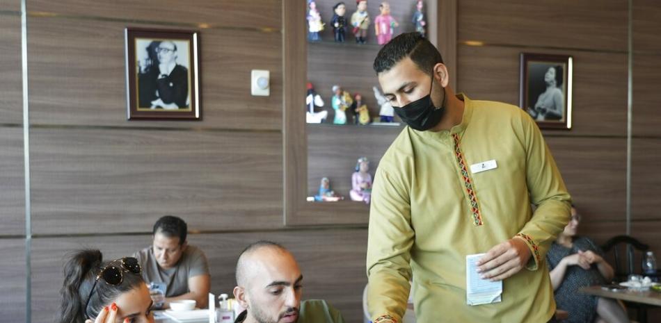Ali el-Sayyed Mohammed toma un pedido a clientes en el restaurante Hadoota Masreya en Dubái, Emiratos Árabes Unidos, el 5 de septiembre de 2022. Mohammed se marchó de su localidad natal de Beheira, en el Delta del Nilo, para instalarse en Dubái con la esperanza de ganarse la vida. Mohammed, de 26 años, dijo que mantiene a su madre y sus hermanas en casa. (AP Foto/Malak Harb)