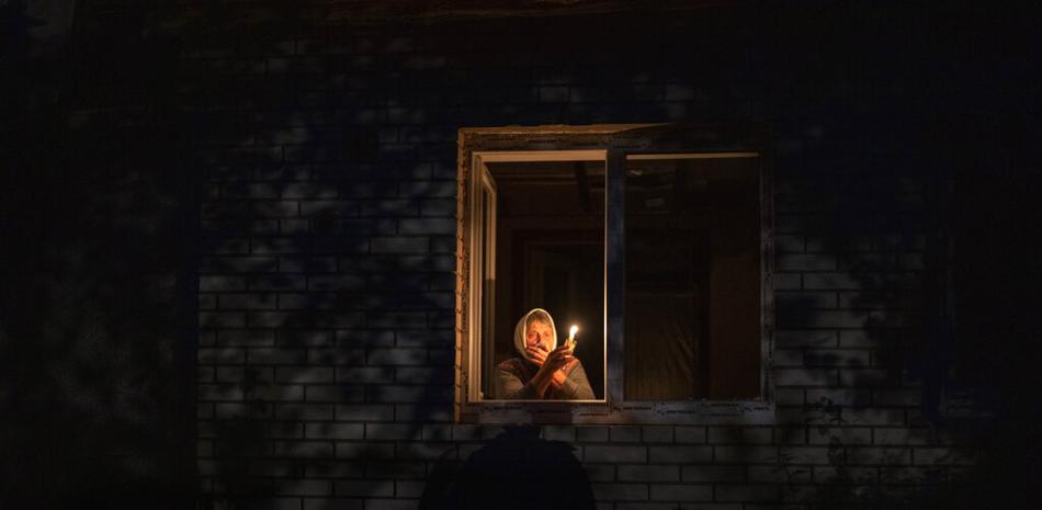 Catherine, de 70 años, mira por la ventana mientras se ilumina con una vela dentro de su casa durante un apagón, el jueves 20 de octubre de 2022, en Borodyanka, en la región de Kiev, Ucrania. AP.