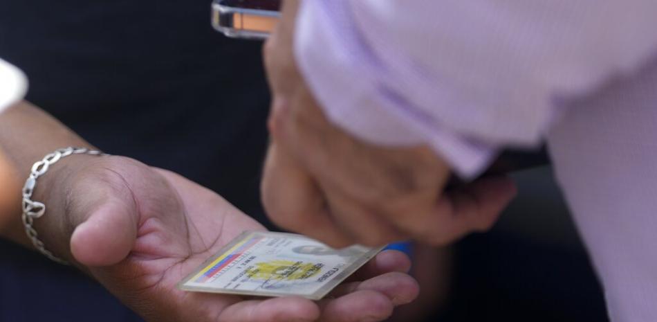 Un migrante venezolano muestra su tarjeta de identificación a un funcionario venezolano antes de abordar un autobús al Aeropuerto Internacional de Tocumen para regresar a Venezuela. AP