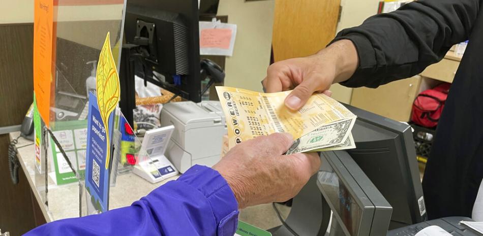 Djuan Davis, detrás del mostrador de lotería de un establecimiento Pick 'n Save en Madison, Wisconsin, entrega boletos de Powerball a Arpad Jakab, electricista retirado y que dijo que los compraba por primera vez. El bote de la lotería Powerball alcanzó hace poco un récord de 1.600 millones de dólares. (AP Foto/Harm Venhuizen)