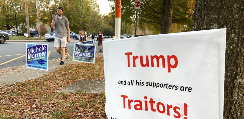 Una familia pasa junto a un cartel que critica al expresidente Donald Trump frente a un lugar de votación anticipada en Wake Forest, Carolina del Norte, el viernes 4 de noviembre de 2022. AP.