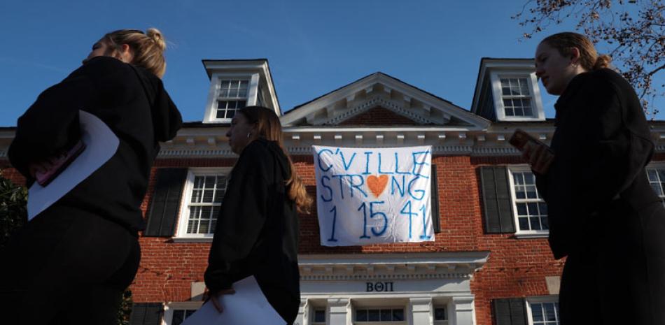 Dos estudiantes pasan frente a una casa de fraternidad con una pancarta que recuerda a tres jugadores de fútbol de la Universidad de Virginia asesinados. AFP/