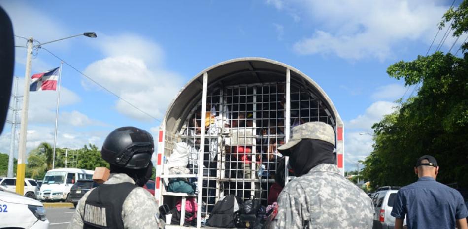 Dos oficiales de Migración observan atentos frente a una unidad repleta de indocumentados haitianos arrestados durante operativos. Después de su detención, estos son llevados a un centro de depuración y aquellos sin estatus legal son devueltos a su país. JA. DONADO