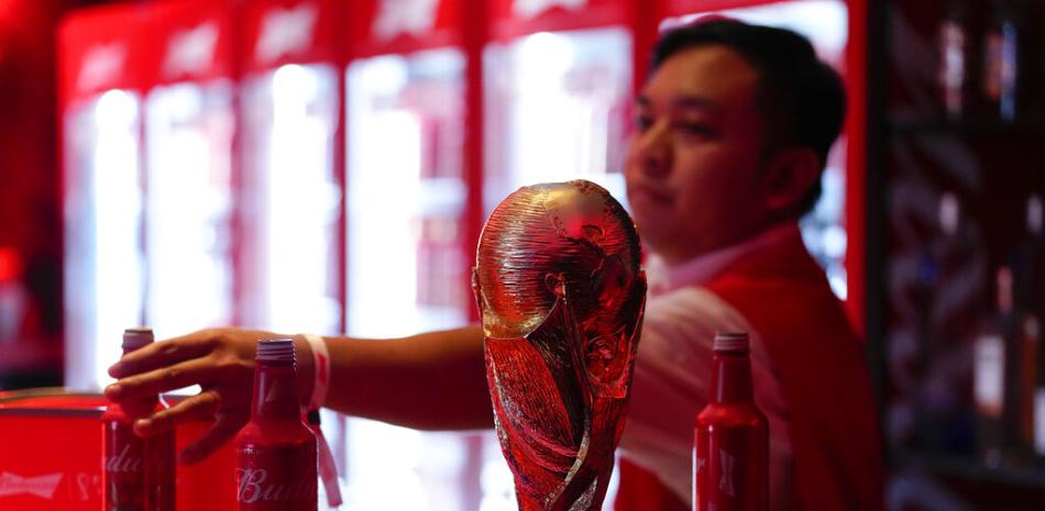 Un cantinero saca botellas de cerveza Budweiser del bar cerca de una réplica del trofeo de la Copa Mundial de la FIFA en una fiesta oficial de fanáticos del fútbol de EE. UU. en el Budweiser World Club, en Doha, el domingo 20 de noviembre de 2022.
