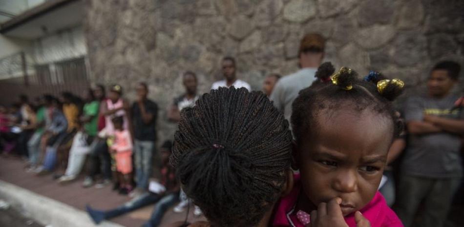 Una haitiana que carga a su hija mientras espera con otras personas afuera de una oficina de asistencia a migrantes en la ciudad de Tapachula, estado de Chiapas, donde pretende conseguir documentos que le permitan permanecer en México, el 20 de junio de 2019. AP