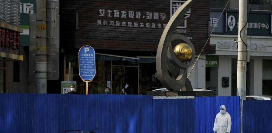 Un trabajador con equipo de protección observa al tiempo que residentes se congregan cerca de las barreras metálicas instaladas en torno a restaurantes que fueron cerrados como parte de los controles contra el COVID-19, en Beijing, el 10 de noviembre de 2022. AP