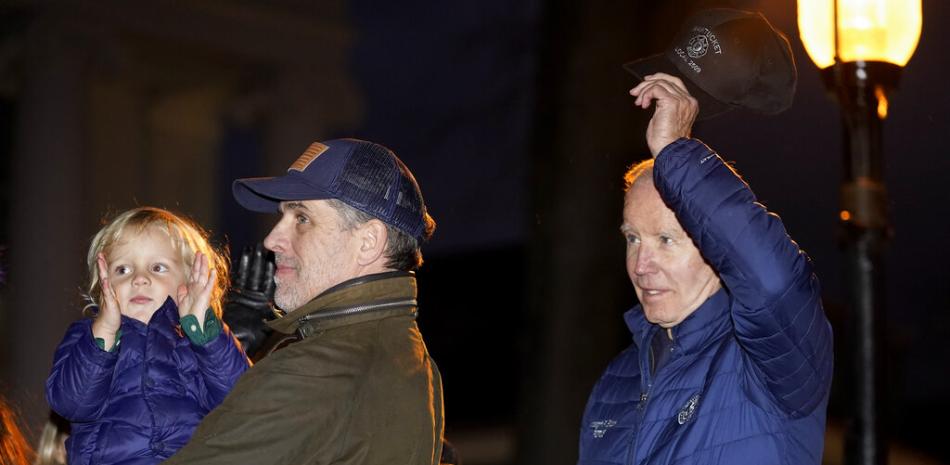 El presidente Joe Biden se quita el sombrero cuando es reconocido durante la ceremonia anual de iluminación del árbol de Navidad en Nantucket, Massachusetts, el viernes 25 de noviembre de 2022. Hunter Biden sostiene a su hijo Beau Biden a la izquierda. (Foto AP/Susan Walsh)