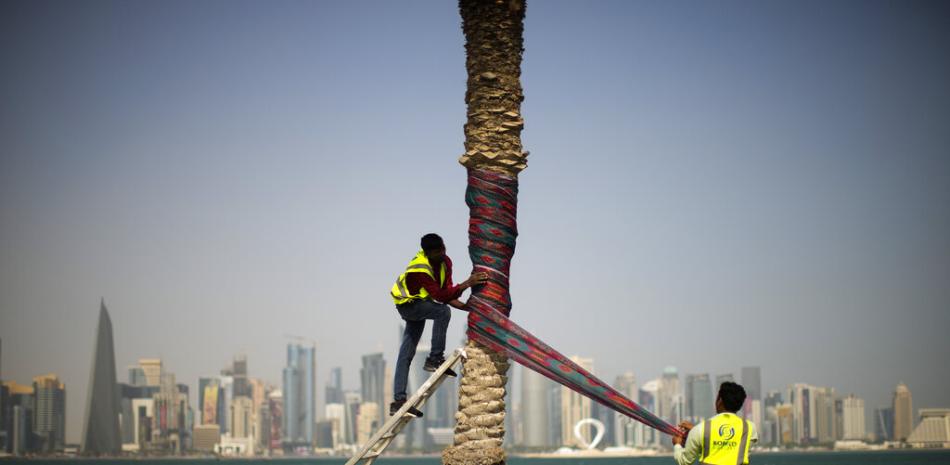 Los trabajadores envuelven una palmera con tela como decoración en el paseo marítimo de Corniche durante el día de inicio de la Copa del Mundo, en Doha, Qatar, el domingo 20 de noviembre de 2022.