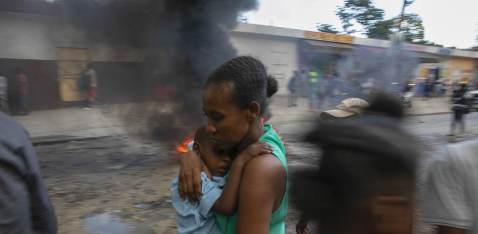 Una madre carga a su hijo mientras corre frente a una barricada en llamas durante una protesta contra el gobierno en Puerto Príncipe, Haití, el viernes 18 de noviembre de 2022. (Foto AP/Odelyn Joseph)