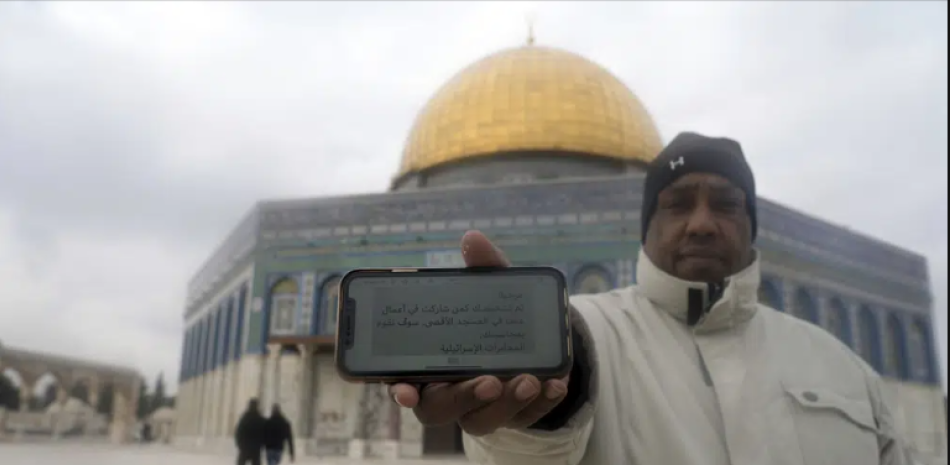 Un musulmán de pie en el complejo de la Mezquita de Al-Aqsa en la zona antigua de Jerusalén muestra en su celular un mensaje amenazante que ha recibido, el 29 de enero de 2022. El mensaje, firmado como "Inteligencia israelí", dice "¡Hola! Se le ha identificado como participante en actos de violencia en la Mezquita de Al-Aqsa y haremos que rinda cuentas". (AP Foto/Mahmoud Illean)