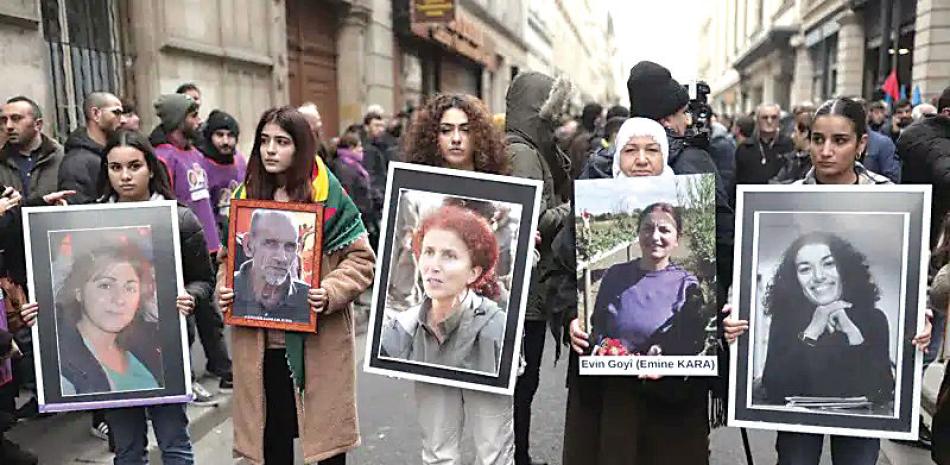 Activistas kurdas con retratos de víctimas en el lugar donde tres mujeres kurdas fueron asesinadas en 2013, en París el 26 de diciembre de 2022.  AP