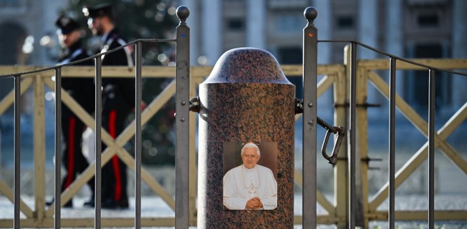 Esta fotografía tomada fuera del Vaticano, el 31 de diciembre de 2022, muestra una imagen del fallecido Papa Benedicto XVI, tras el anuncio de su muerte. Fuente: AFP.