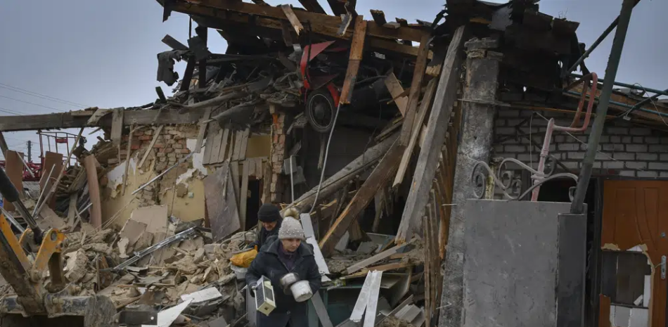 Personas cargan sus pertenencias al dejar sus casas destrozadas en el ataque con cohete ruso del sábado en Zaporiyia, Ucrania, el domingo 1 de enero de 2023. (AP Foto/Andriy Andriyenko)