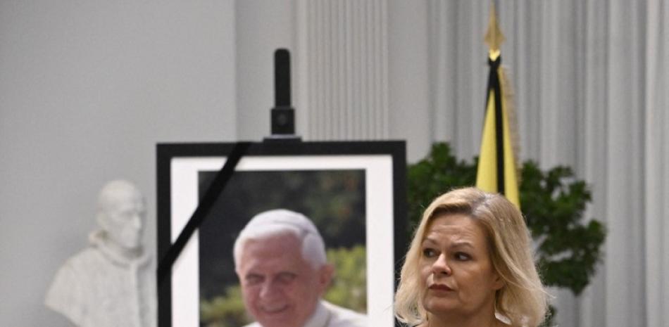 La ministra del Interior alemana, Nancy Faeser, se va después de firmar un libro de condolencias al difunto Papa emérito Benedicto XVI, visto en un retrato al fondo, en la Nunciatura Apostólica en Alemania. Foto de AFP