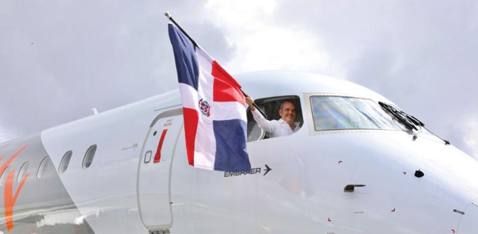 Abinader levanta la bandera nacional a través de una ventanilla de piloto de avión de la empresa Embraer.