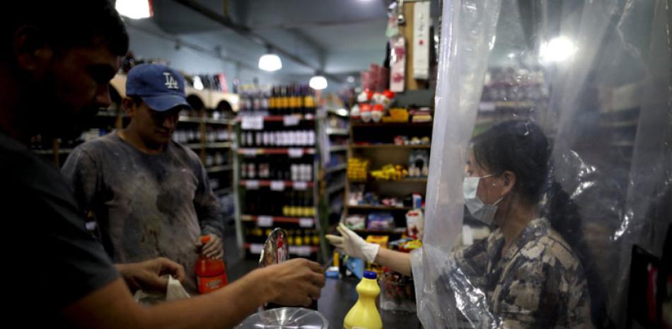 Una vendedora de supermercado atiende a un cliente tras una cortina de plástico como precaución contra el nuevo coronavirus en Buenos Aires, el 16 de marzo de 2020. AP