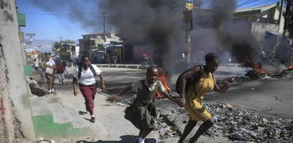 Una mujer y su hija pasan corriendo frente a una barricada levantada por la policía en protesta por el mal gobierno policial en Puerto Príncipe, Haití, el 26 de enero de 2023. Las casi 200 pandillas de Haití se han aprovechado del caos, luchando por el control. (AP)